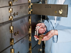 Pearls and watch in front of an open safe deposit box