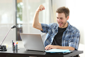 Young adult on computer with fist in the air