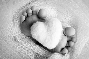 baby feet swaddled in a blanket next to a cotton heart